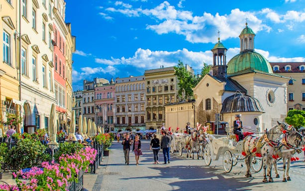 Krakow street with horse-drawn carriages and historic buildings on a day tour from Warsaw.