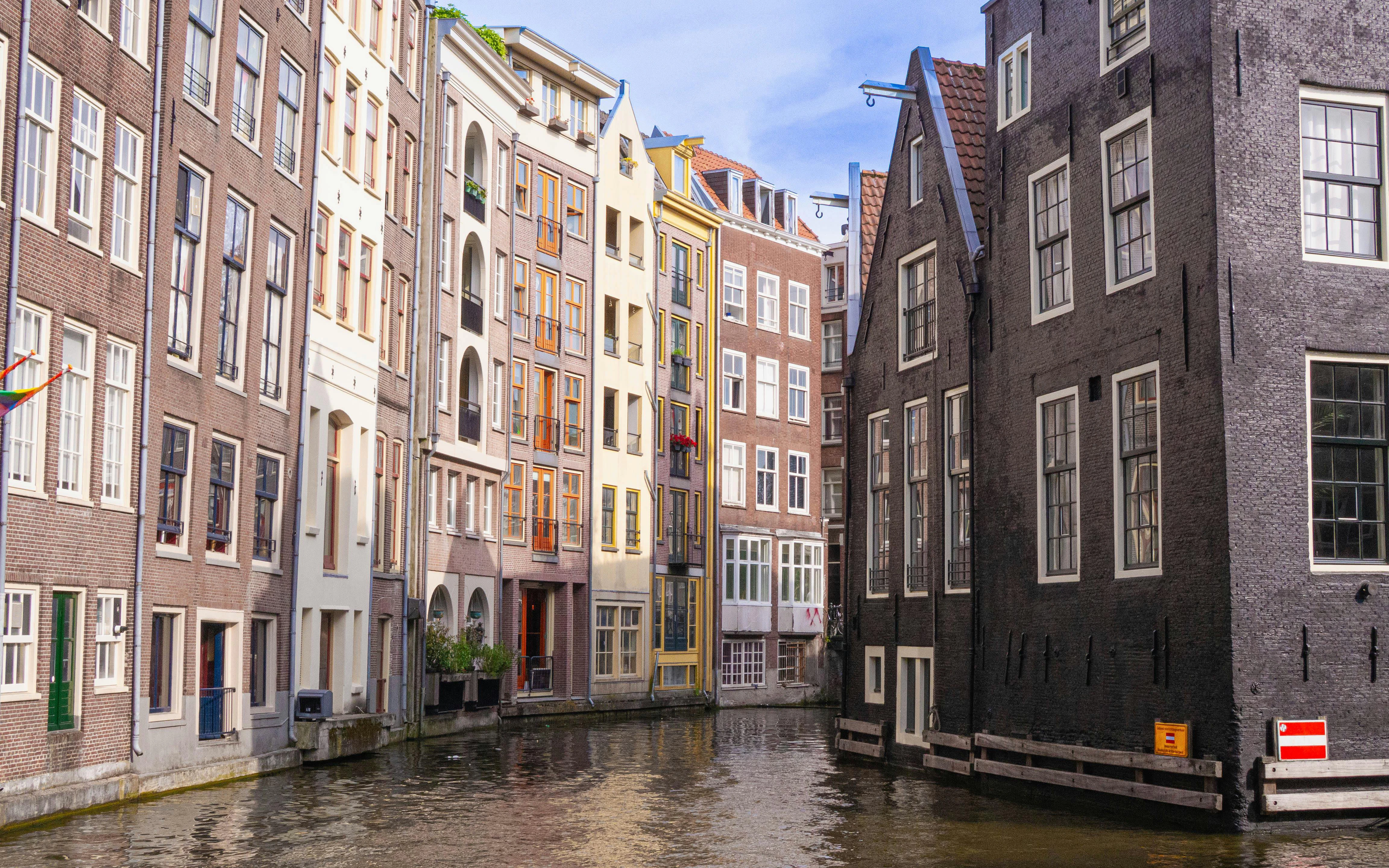 Tall heritage houses with colorful facades along Amsterdam's Damrak and Kop Zeedijk canal.