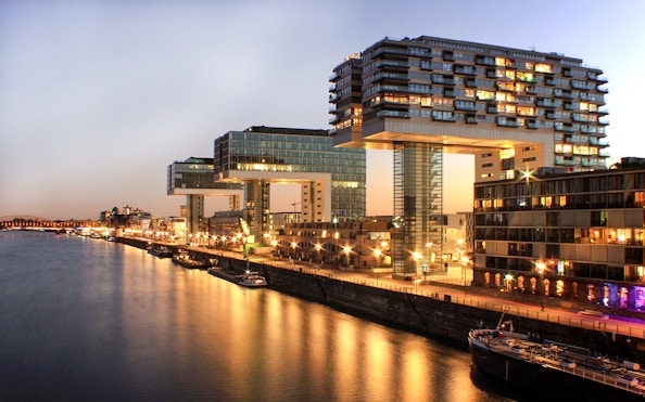 Evening view of Cologne's Rheinauhafen district with illuminated Kranhäuser buildings.