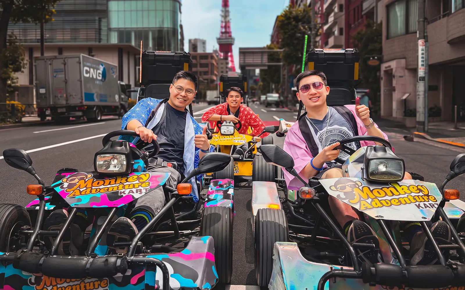 Go-kart riders in costumes on Tokyo street with Tokyo Tower in background.