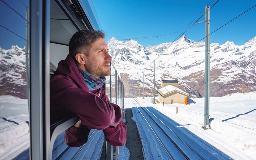 Man enjoying scenic view from train to Gornergrat, snowy mountains in background, Zermatt.