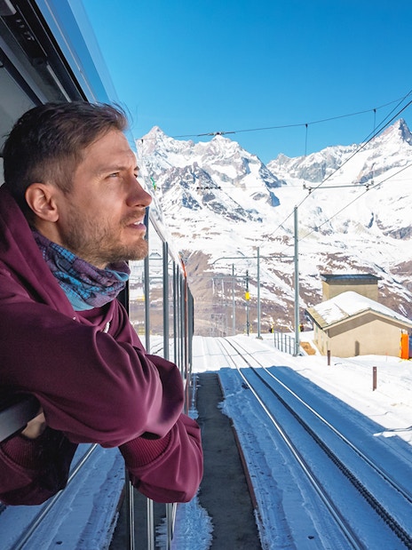 Man enjoying scenic view from train to Gornergrat, snowy mountains in background, Zermatt.