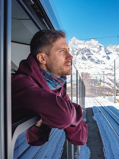 Man enjoying scenic view from train to Gornergrat, snowy mountains in background, Zermatt.