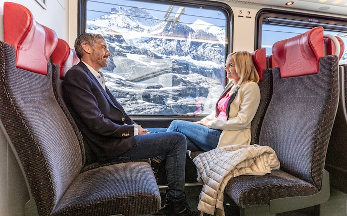 Passengers enjoying scenic views on Jungfraujoch Railway with snowy mountains in background.
