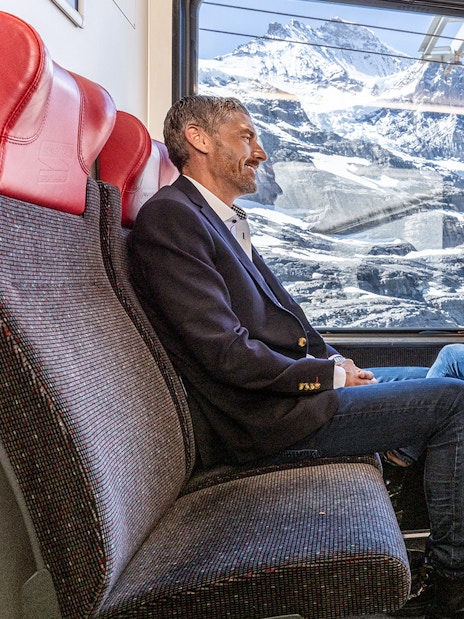 Passengers enjoying scenic views on Jungfraujoch Railway with snowy mountains in background.