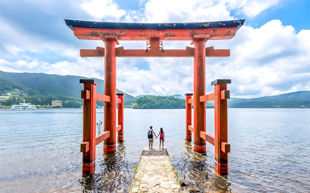 Couple standing at Hakone Torii Gate overlooking Lake Ashi, Japan.
