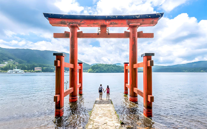 Couple standing at Hakone Torii Gate overlooking Lake Ashi, Japan.