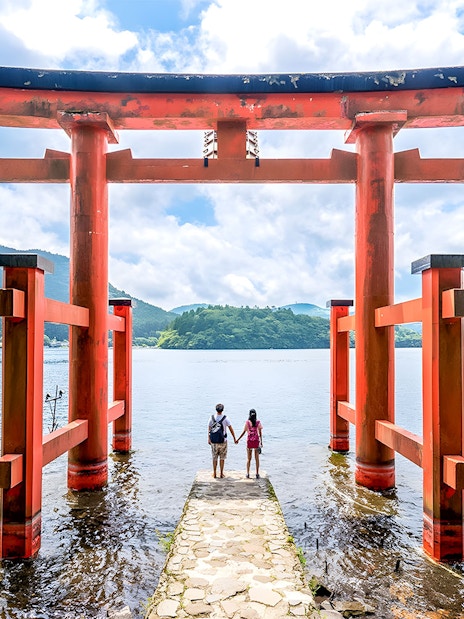 Couple standing at Hakone Torii Gate overlooking Lake Ashi, Japan.