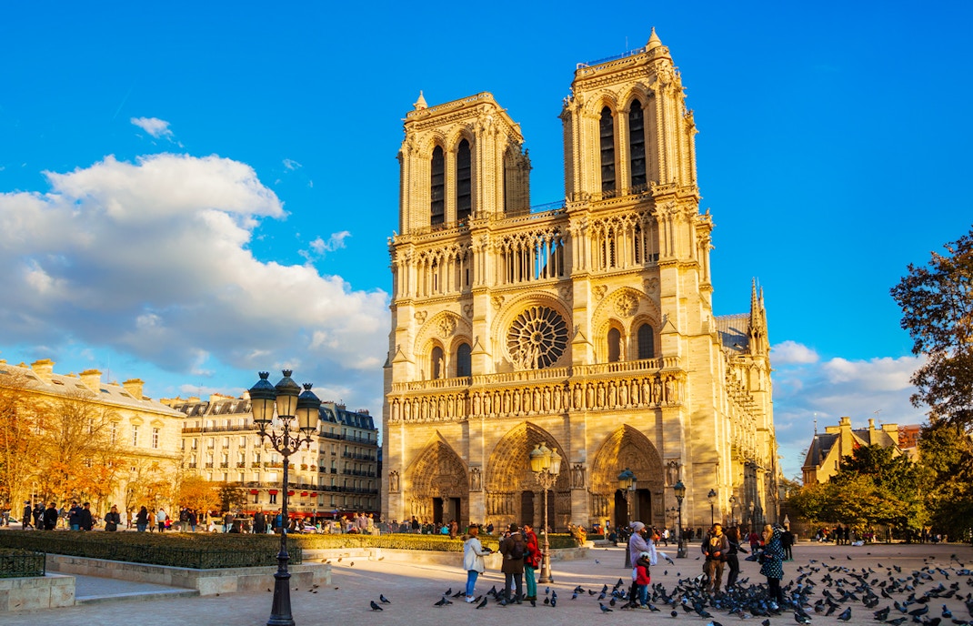 Notre Dame de Paris cathedral illuminated during golden hour with people in the foreground.