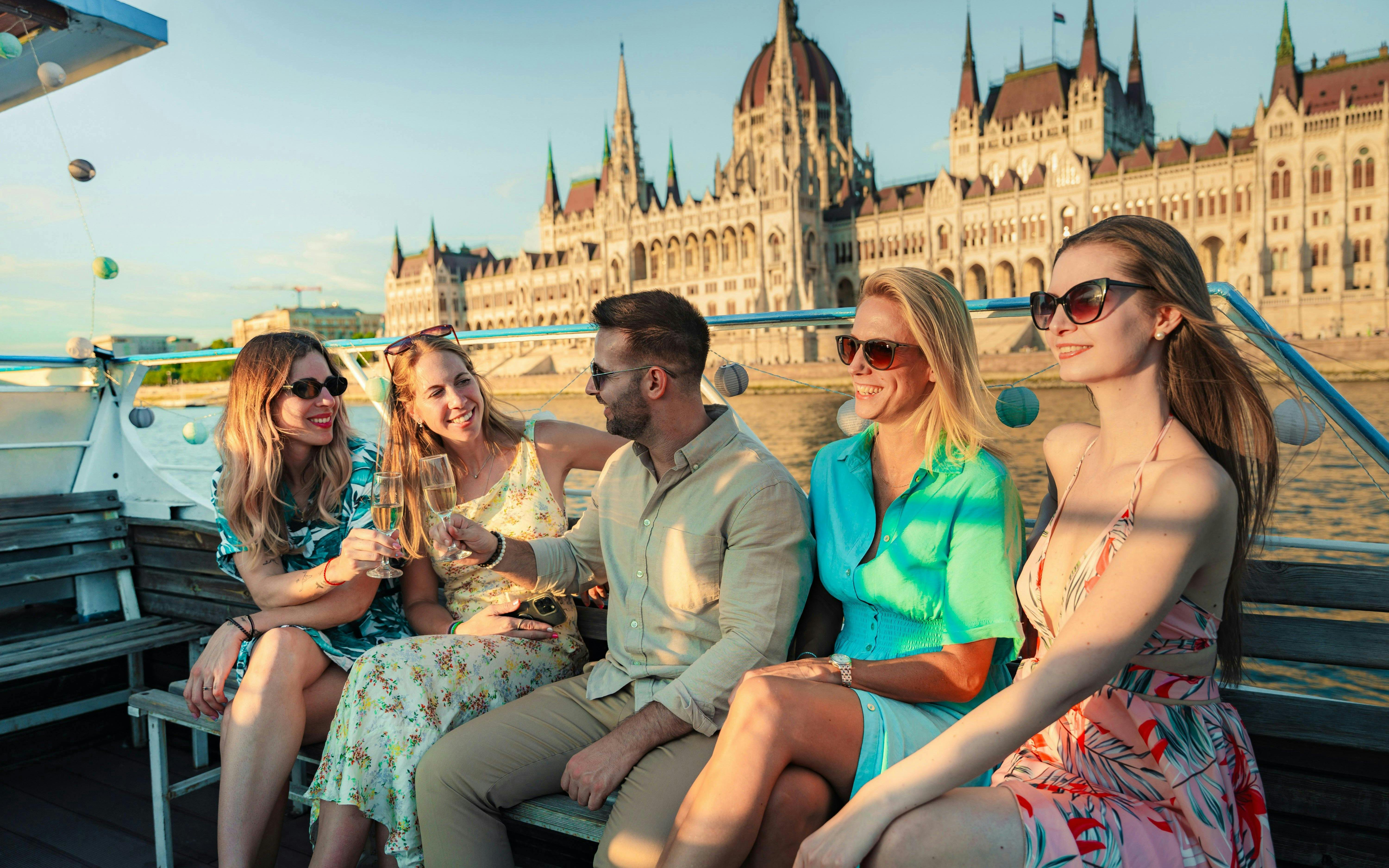 Tourists enjoying drinks on Budapest daytime hop-on hop-off cruise with Parliament view.