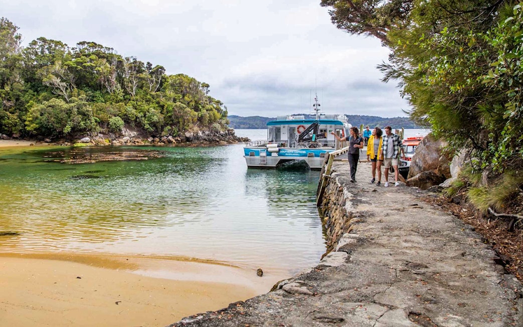 Tourists disembarking from boat at Ulva Island, New Zealand, surrounded by lush greenery.