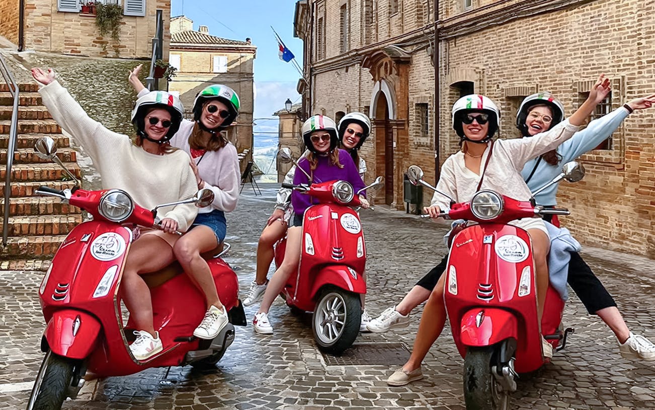 Group enjoying a Free Vespa Tour on red scooters in a historic European town.