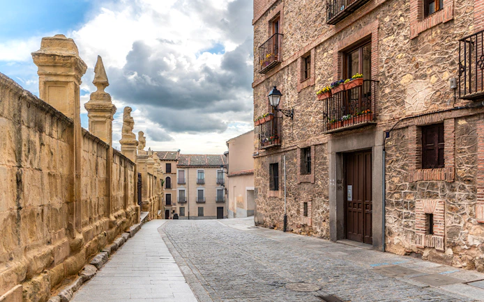 Cobblestone street in the Jewish Quarter, Segovia, with historic stone buildings and ornate balconies.