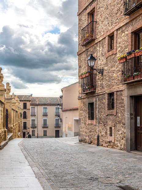 Cobblestone street in the Jewish Quarter, Segovia, with historic stone buildings and ornate balconies.