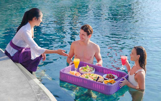 Floating breakfast in pool at Toya Devasya resort with two guests and server.