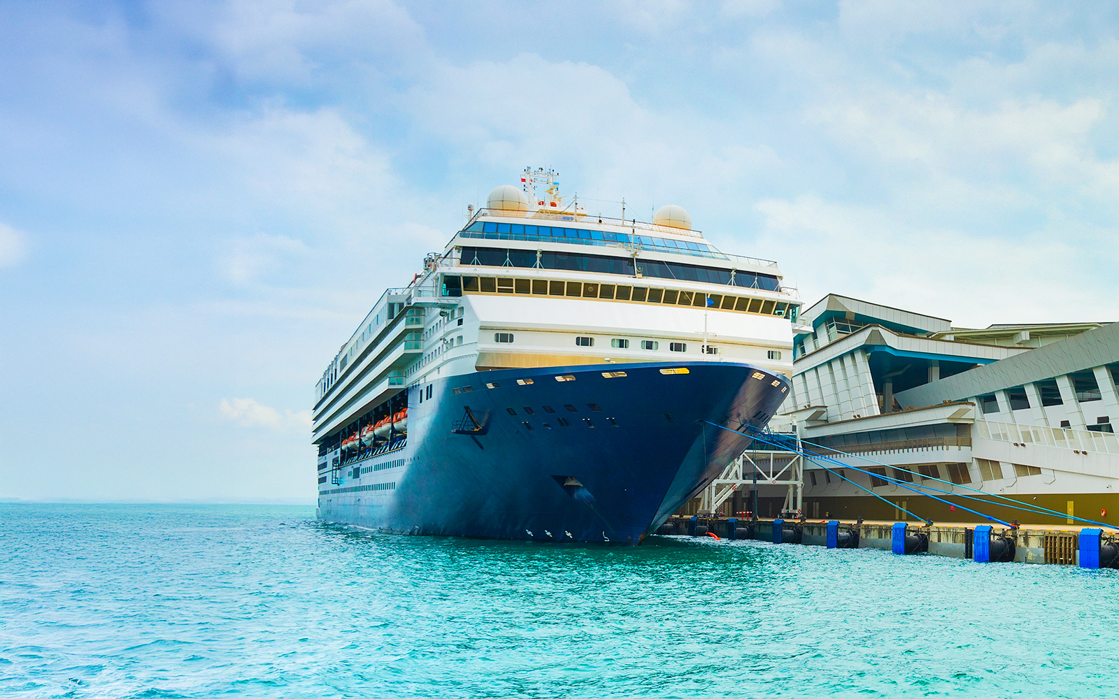 Disney cruise ship docked at Singapore port with city skyline in the background.