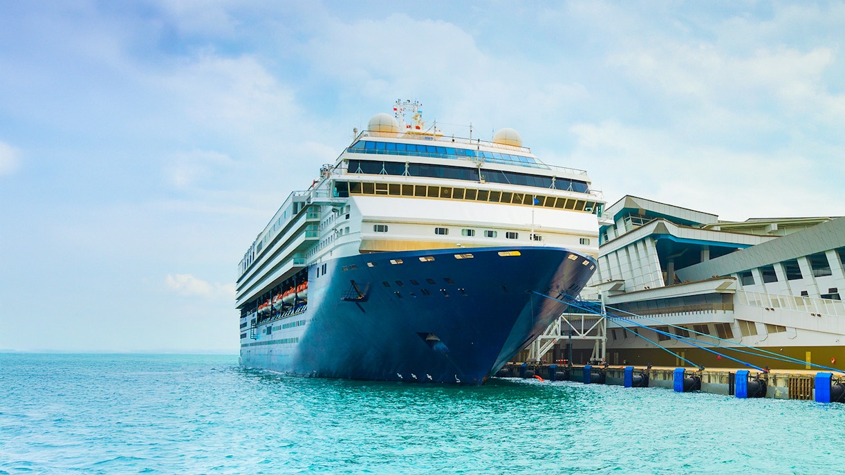 Disney cruise ship docked at Singapore port with city skyline in the background.
