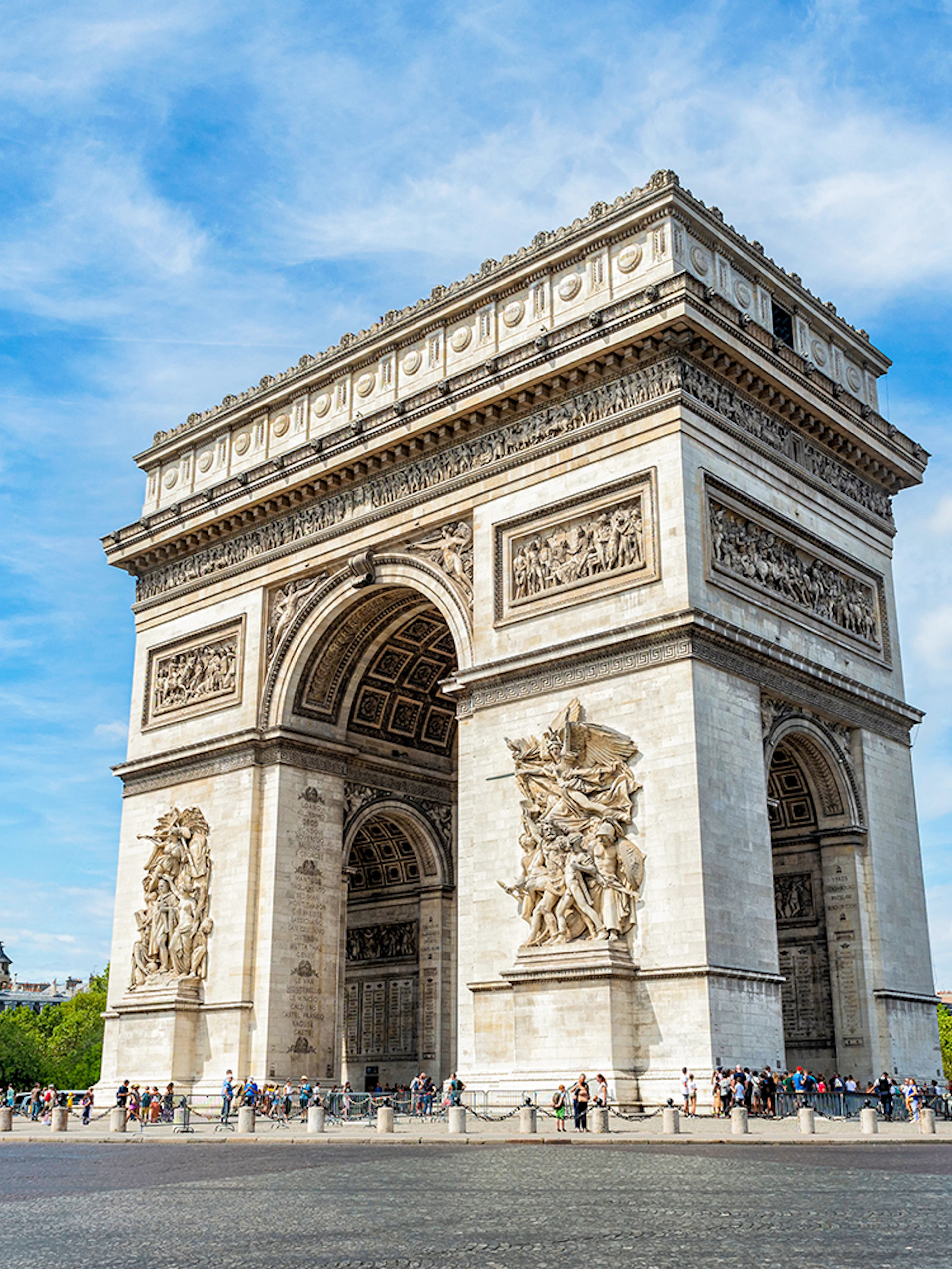 Arc de Triomphe in Paris with tourists and clear blue sky.