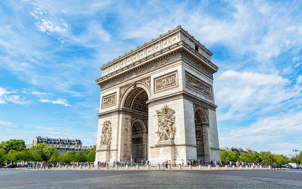 Arc de Triomphe in Paris with tourists and clear blue sky.