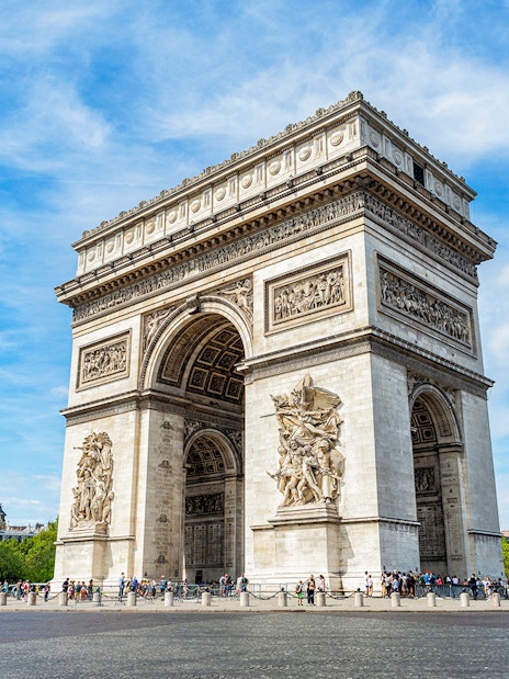 Arc de Triomphe in Paris with tourists and clear blue sky.