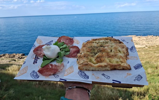 Focaccia bread with local cheese and cured meats by the sea during Polignano a Mare street food tour.