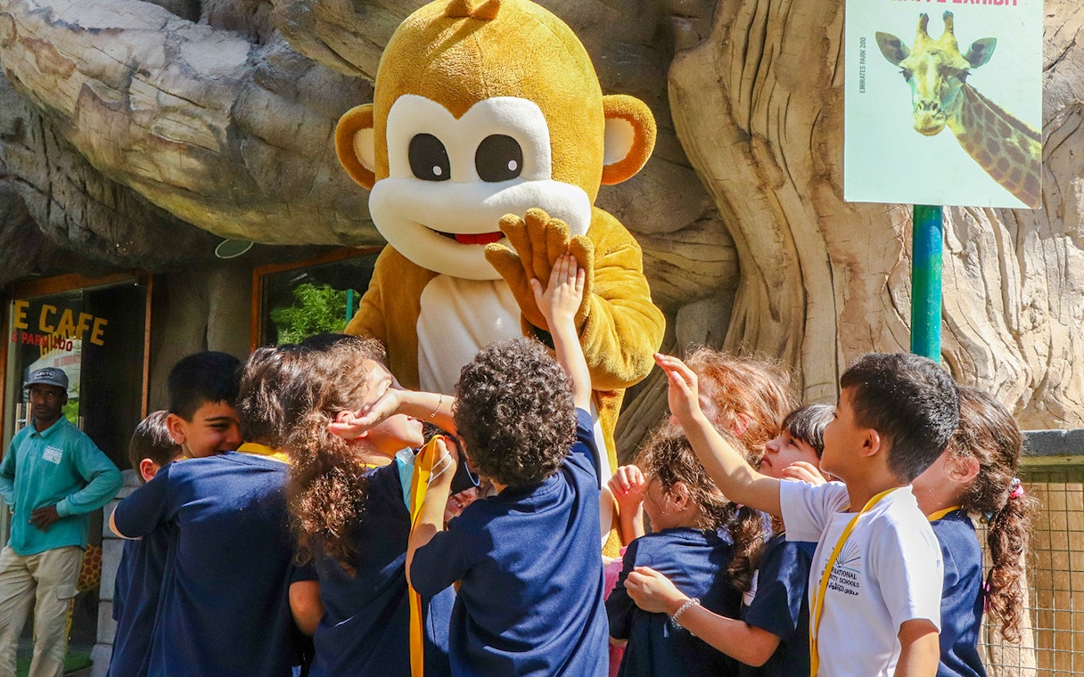 Children interacting with a monkey mascot at a zoo exhibit.