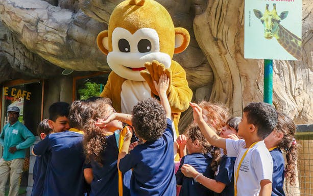 Children interacting with a monkey mascot at a zoo exhibit.