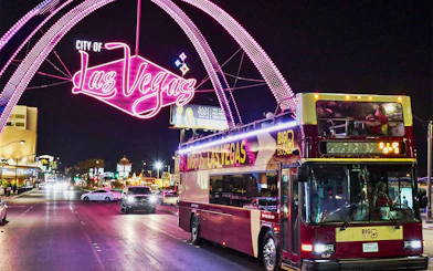Big Bus tour in Las Vegas at night under neon city sign.