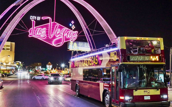 Big Bus tour in Las Vegas at night under neon city sign.