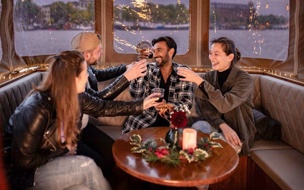 Friends toasting on a cozy Amsterdam Light Festival cruise with festive decor.