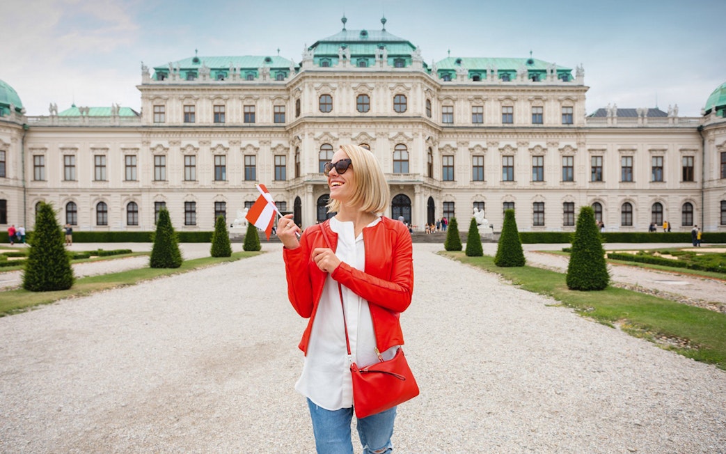 Woman holding a flag in front of Upper Belvedere Palace on a guided tour in Vienna.