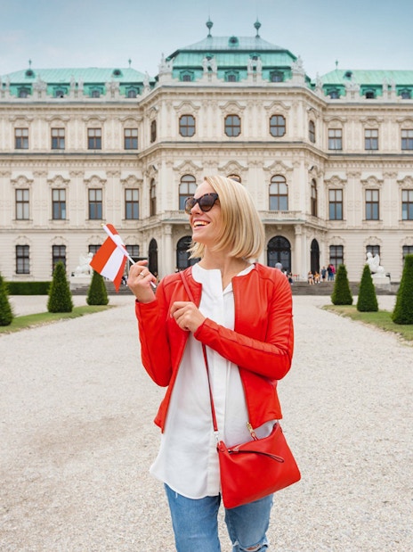 Woman holding a flag in front of Upper Belvedere Palace on a guided tour in Vienna.