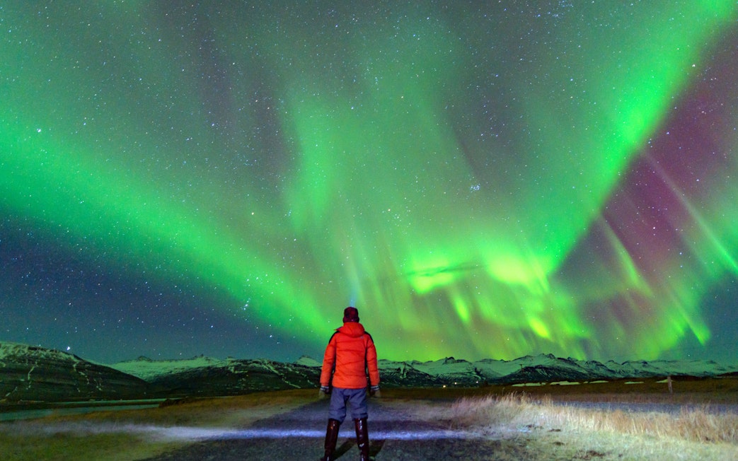 Tourist viewing Northern Lights over snowy landscape in Iceland.