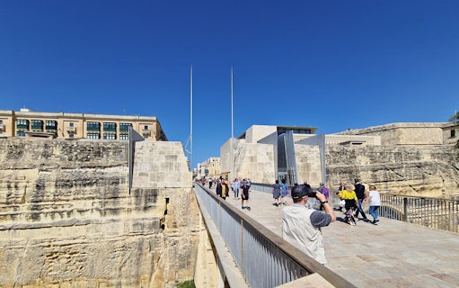 Visitors walking on a bridge towards Valletta's historic city gate during a food tour.