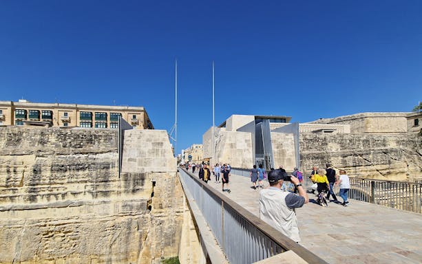 Visitors walking on a bridge towards Valletta's historic city gate during a food tour.