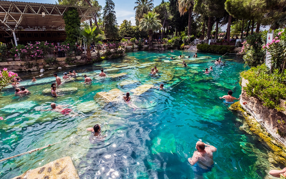 Visitors swimming in the thermal pools of Pamukkale, surrounded by lush greenery.