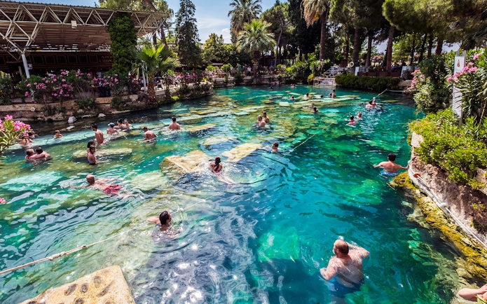Visitors swimming in the thermal pools of Pamukkale, surrounded by lush greenery.