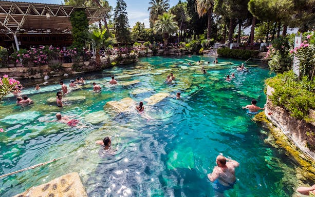 Visitors swimming in the thermal pools of Pamukkale, surrounded by lush greenery.
