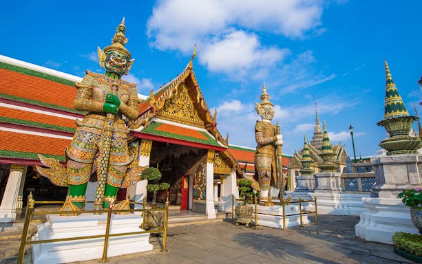 Giant guardian statues at Bangkok's Grand Palace entrance, Wat Phra Chetuphon in background.