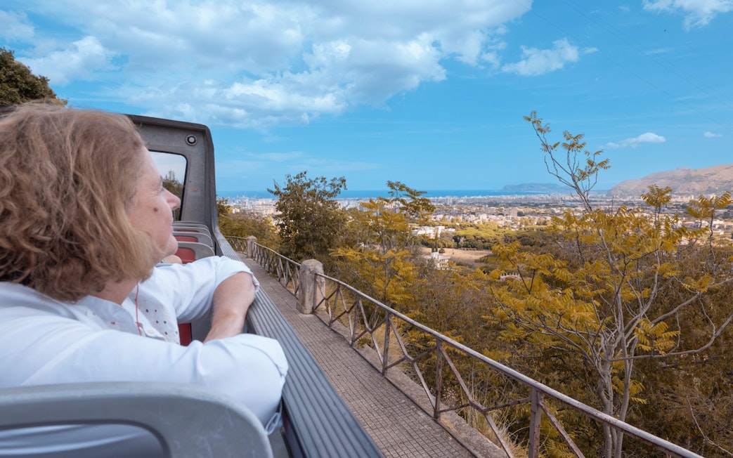 People enjoying the view from a City Sightseeing bus in Palermo, overlooking the cityscape and sea.
