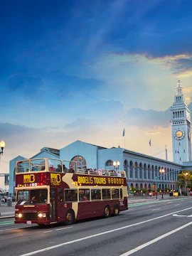 Open-top Big Bus tour passing San Francisco Ferry Building at sunset.