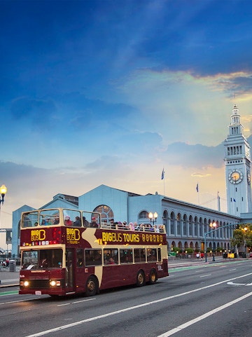 Open-top Big Bus tour passing San Francisco Ferry Building at sunset.