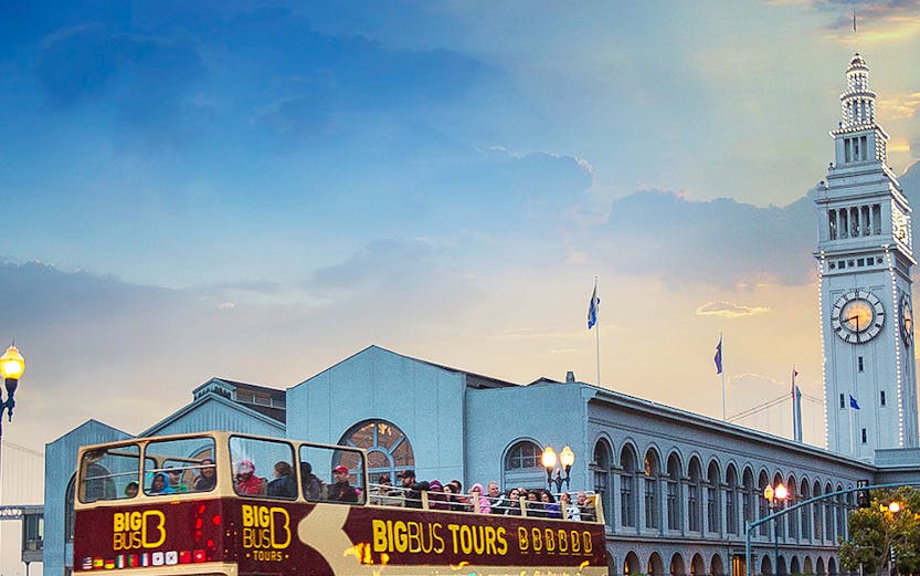 Open-top Big Bus tour passing San Francisco Ferry Building at sunset.