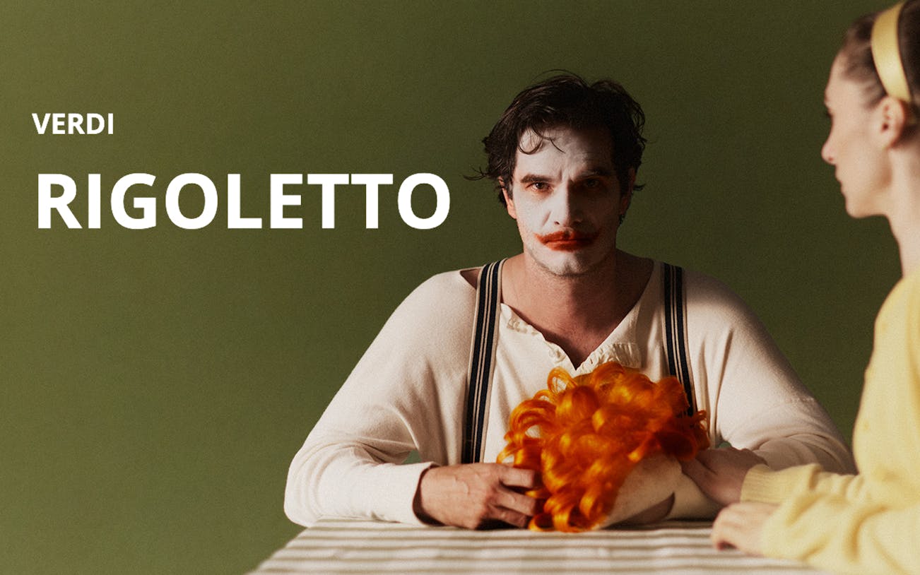 Performer in clown makeup holding a wig, promoting Verdi's Rigoletto.