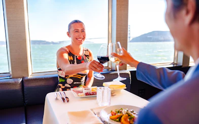 Guests toasting with wine on a San Francisco dinner cruise with a view of the bay.