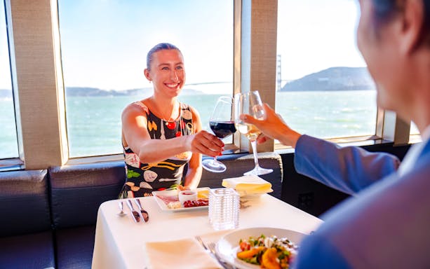 Guests toasting with wine on a San Francisco dinner cruise with a view of the bay.