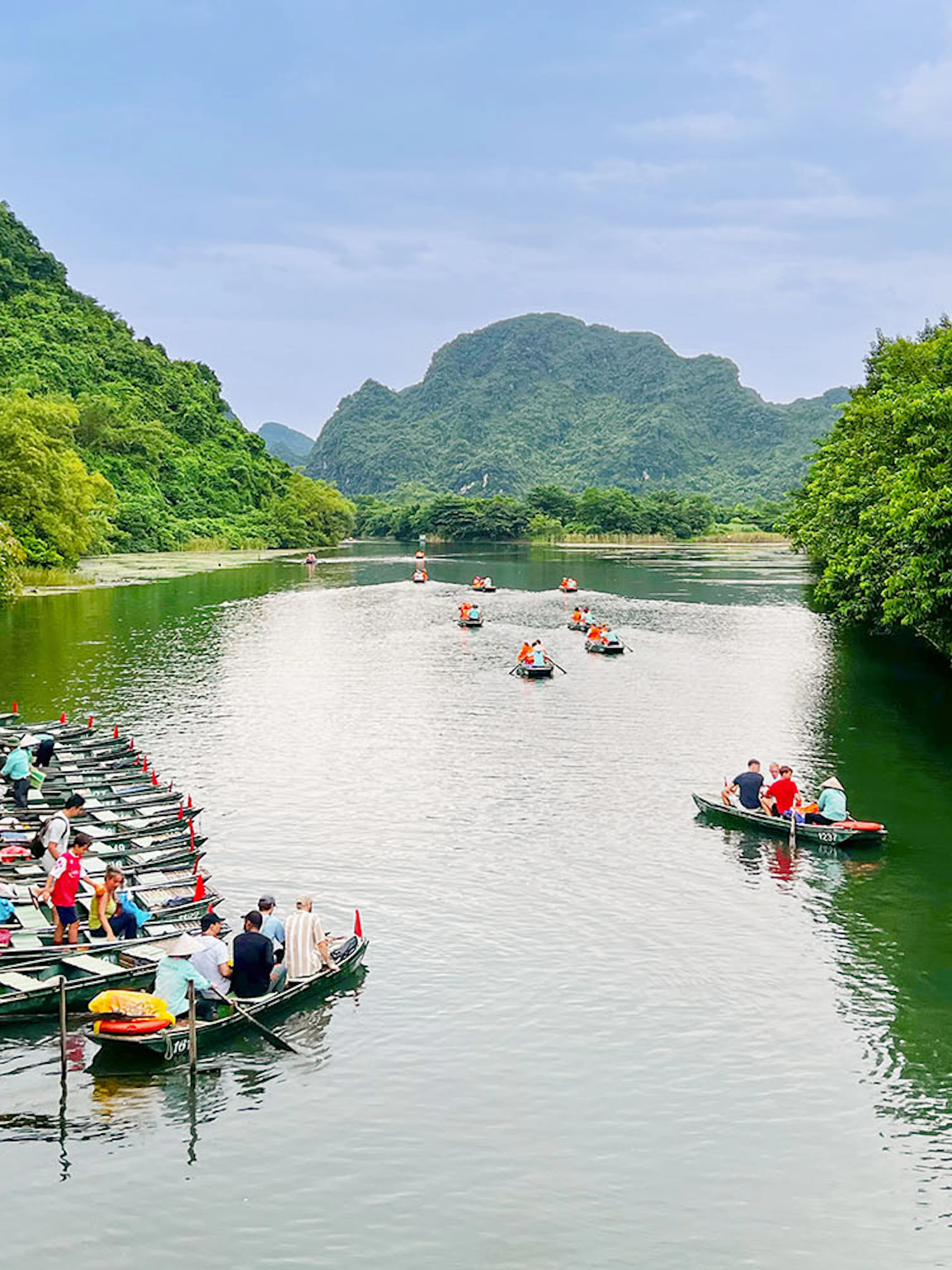 Boat tour on the river at Trang An Landscape Complex, Ninh Binh, Vietnam, surrounded by lush greenery.