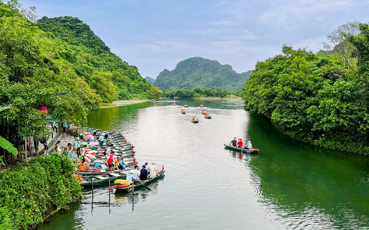 Boat tour on the river at Trang An Landscape Complex, Ninh Binh, Vietnam, surrounded by lush greenery.