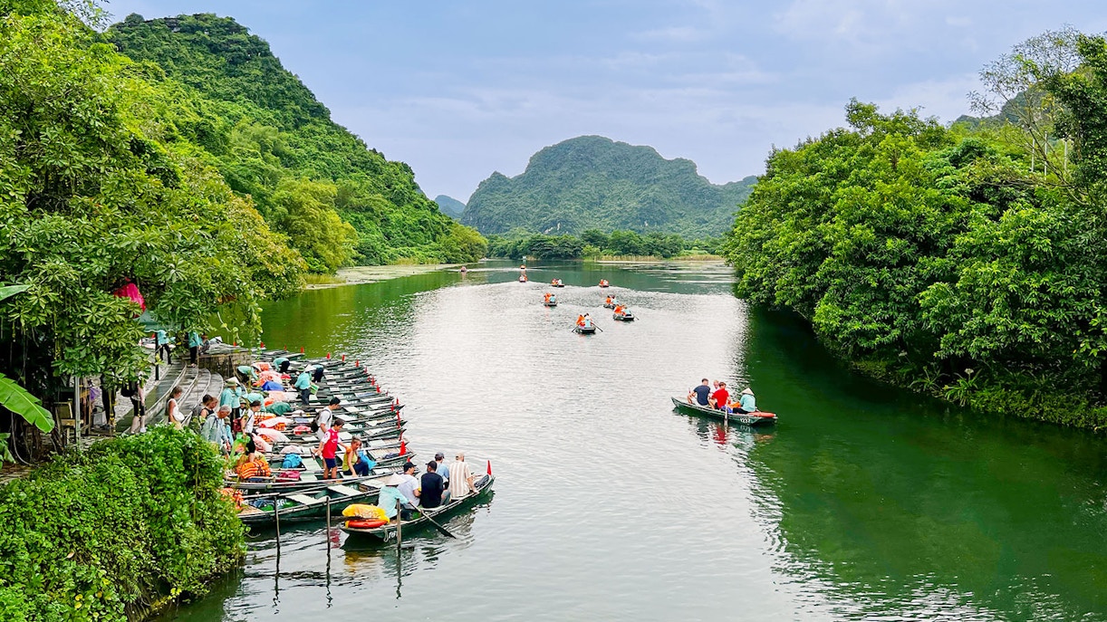 Boat tour on the river at Trang An Landscape Complex, Ninh Binh, Vietnam, surrounded by lush greenery.