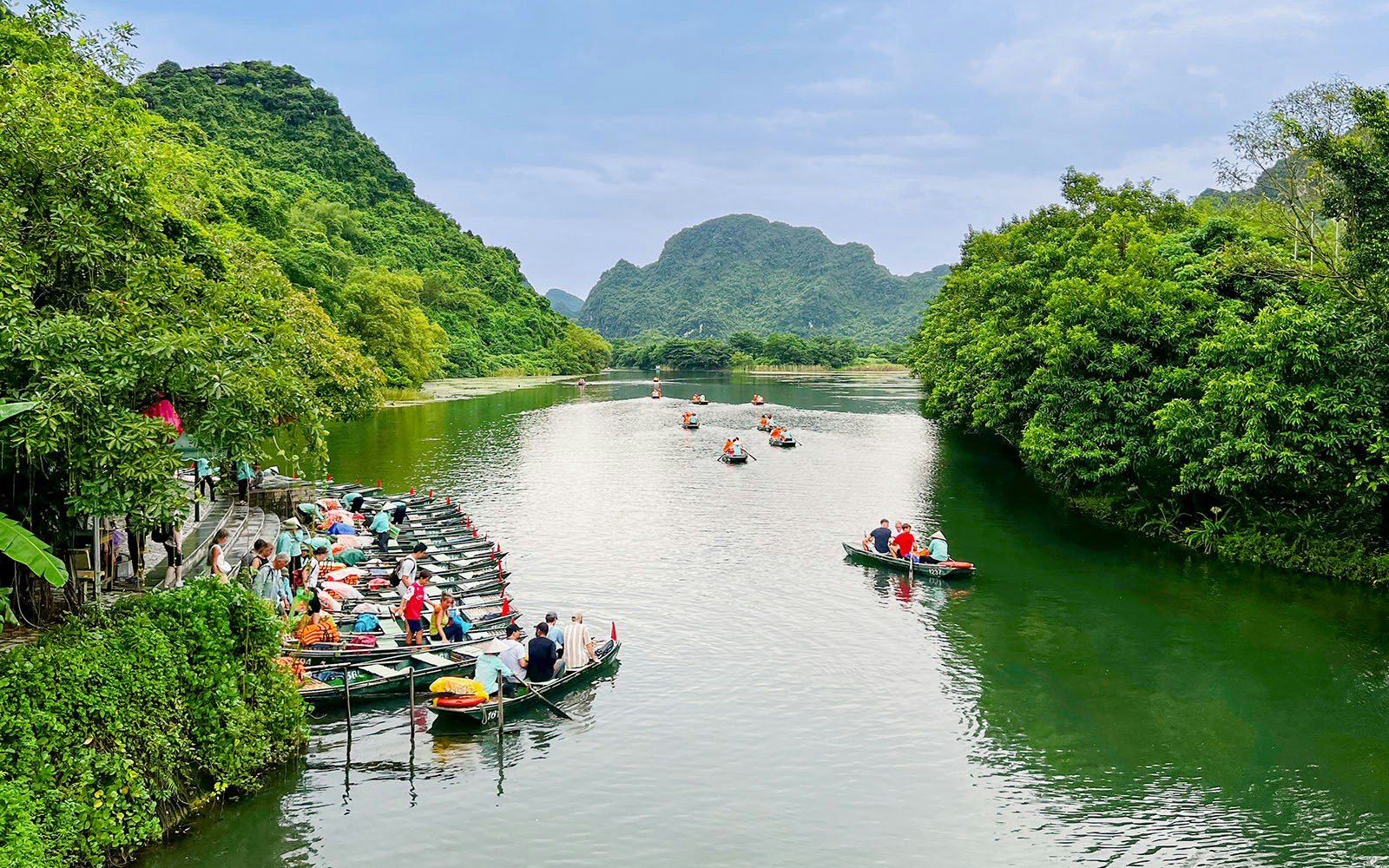 Boat tour on the river at Trang An Landscape Complex, Ninh Binh, Vietnam, surrounded by lush greenery.
